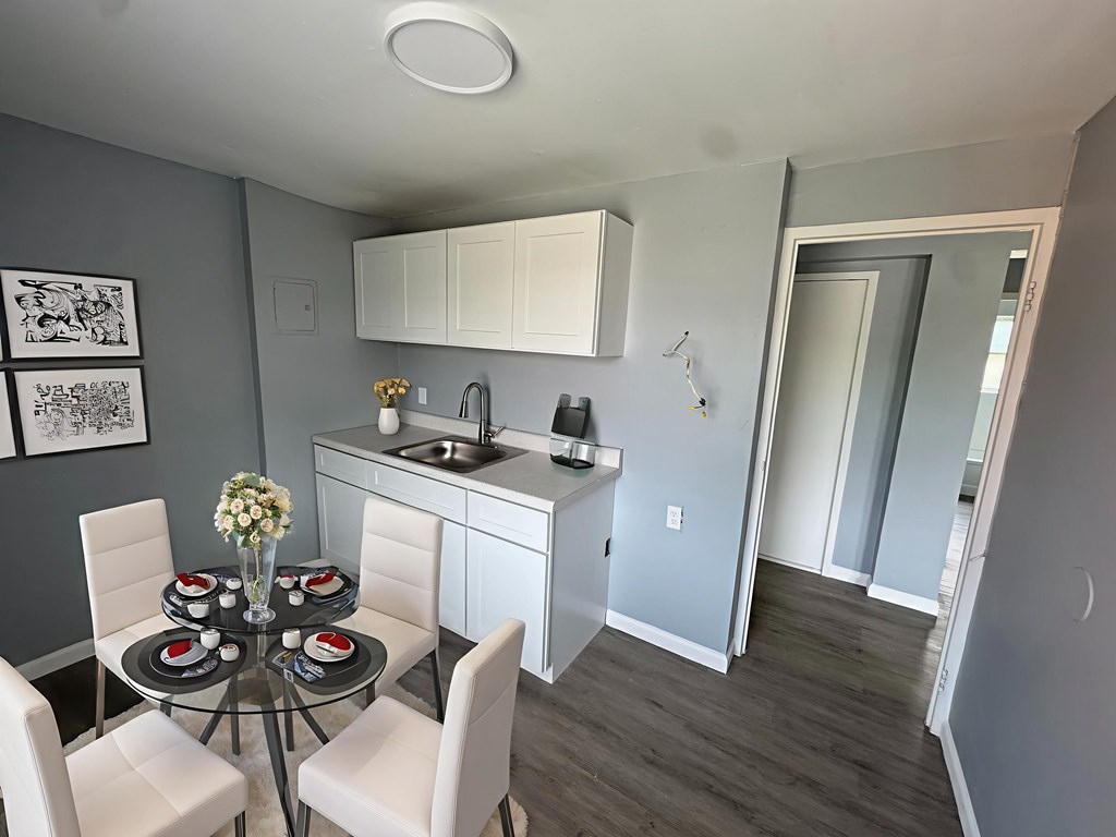A kitchen with a table and chairs in the foreground and a sink and cabinets in the background.