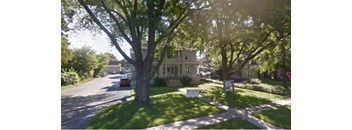 A tree-lined street with a house and a car parked on the side.