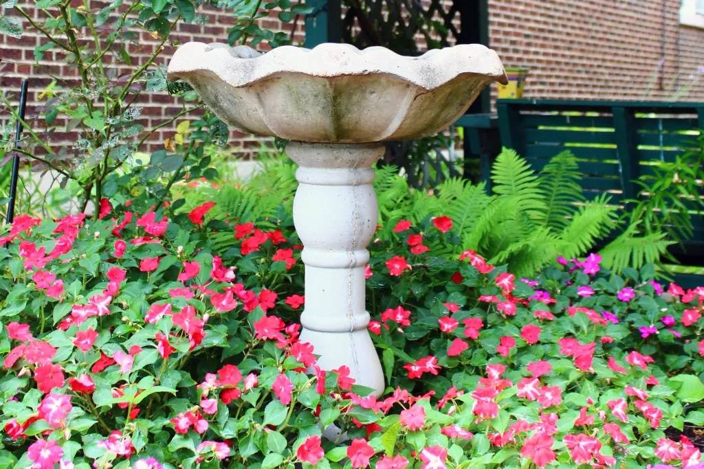 a white bird bath sitting in the middle of a flower garden