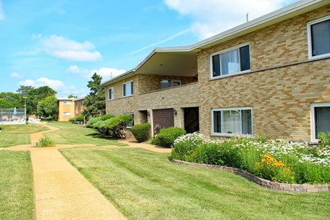 a large brick apartment building with a lawn and flowers in front of it