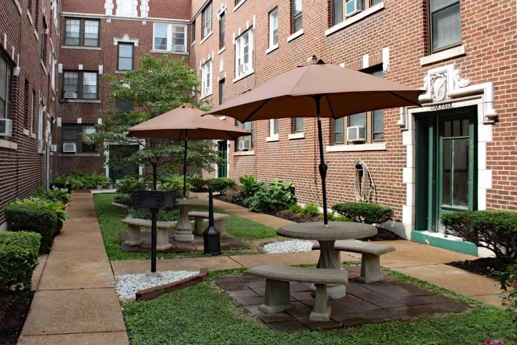 a courtyard with tables and umbrellas in front of a brick building