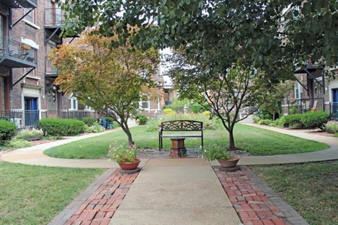 a park with a bench and trees in front of an apartment building