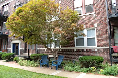 two blue chairs sit on a sidewalk in front of a brick apartment building