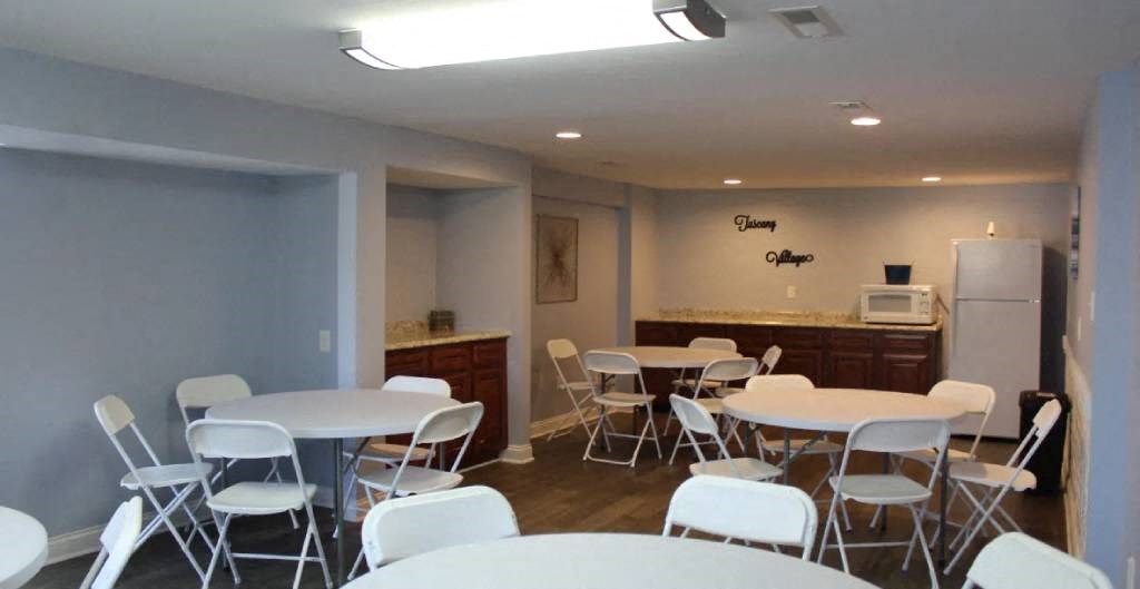 a room with tables and chairs and a kitchen in the background