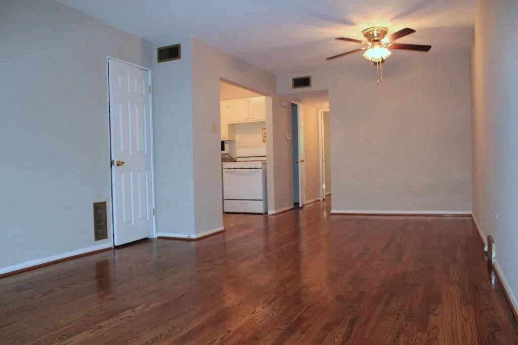 an empty living room with a ceiling fan and a kitchen in the background