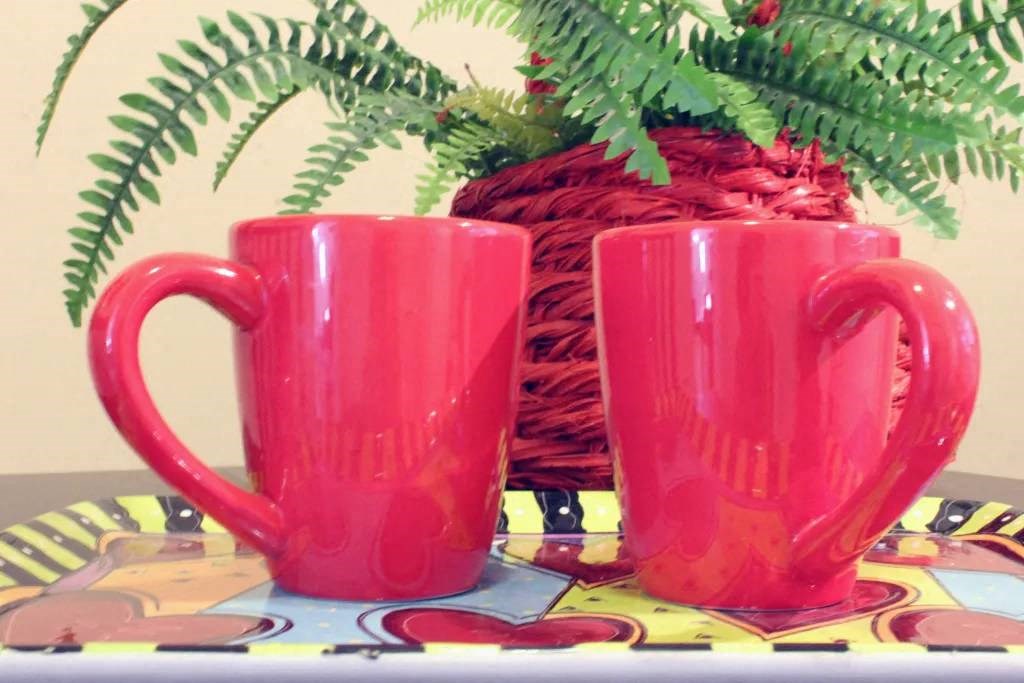 two red cups sitting on a table next to a plant