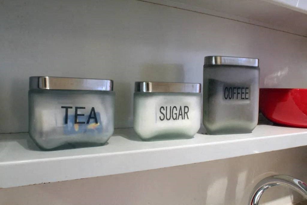 a shelf with three glass containers that say tea sugar and coffee