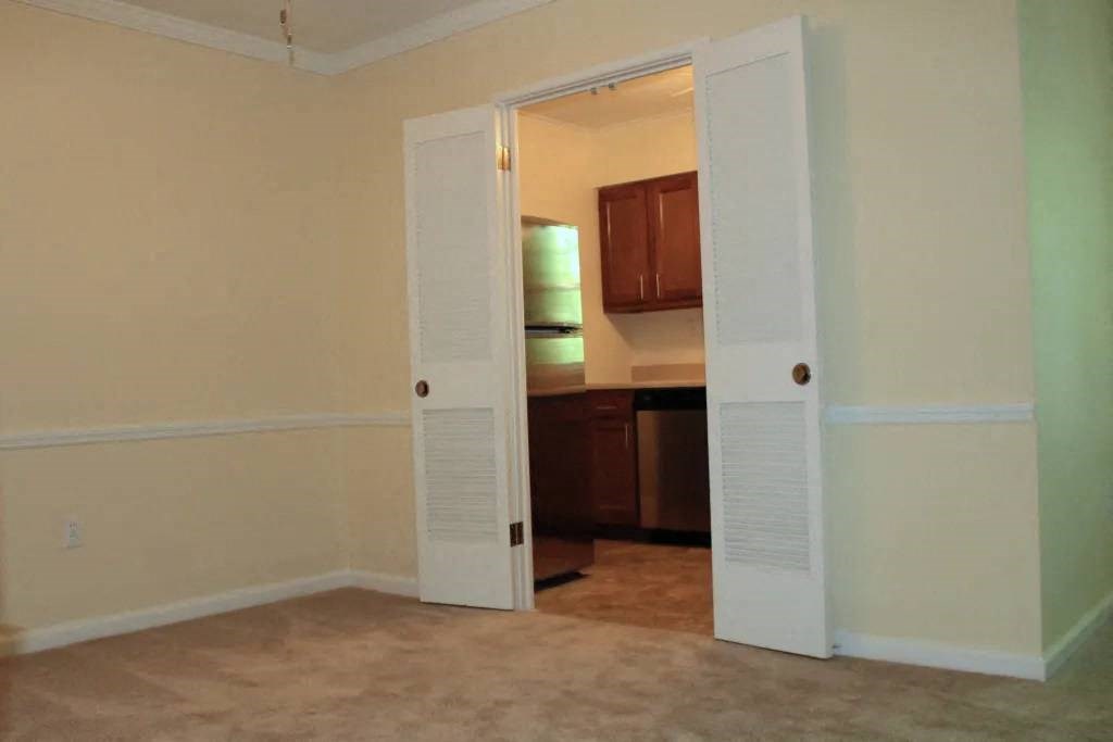 a room with an open door and a kitchen in the background