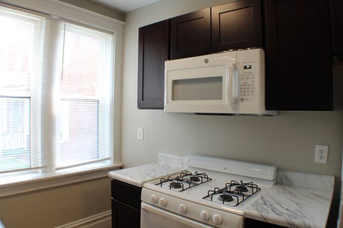 A white microwave oven is mounted above a white gas stove in a kitchen.