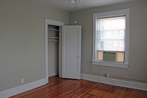 A room with a wooden floor, a white door, and a window with blinds.