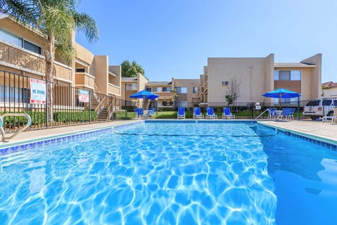 A large swimming pool in front of a building with a fence and umbrellas.