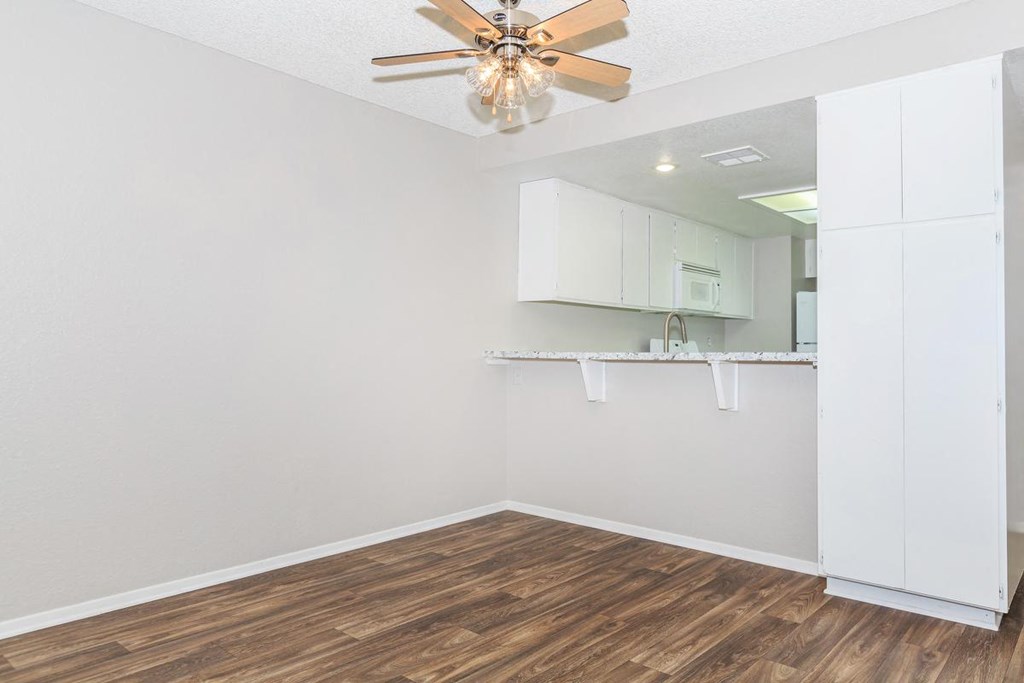 an empty living room with a ceiling fan and a kitchen