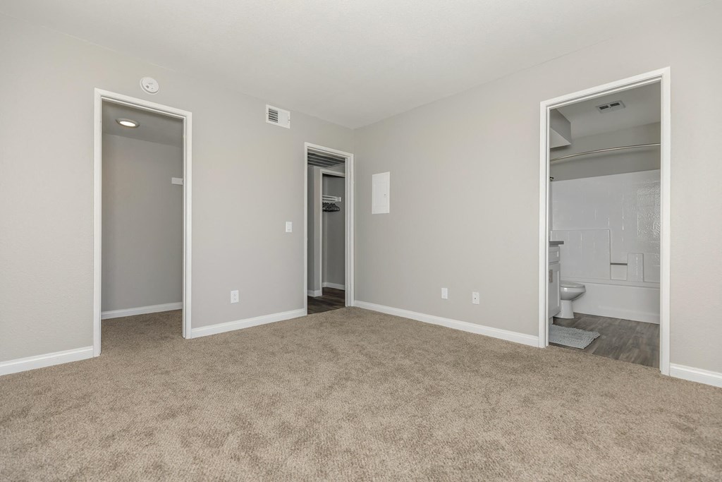 an empty living room with two doors to a bathroom and a closet