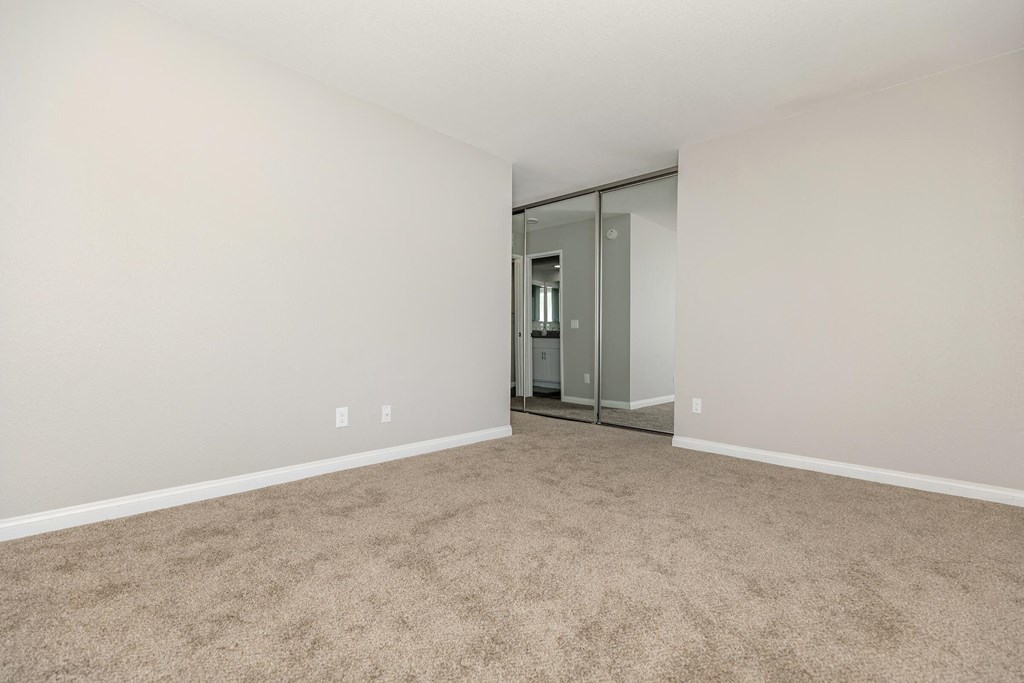 an empty living room with carpet and a mirrored closet