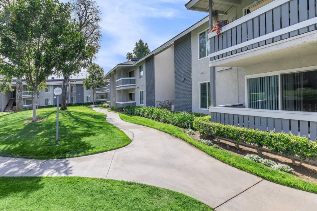 a walkway between two apartment buildings with grass and trees