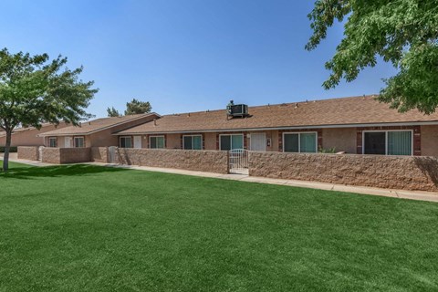 A grassy area in front of a building with a wall and a tree.