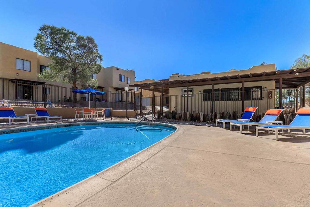 A pool area with sun loungers and a tree.