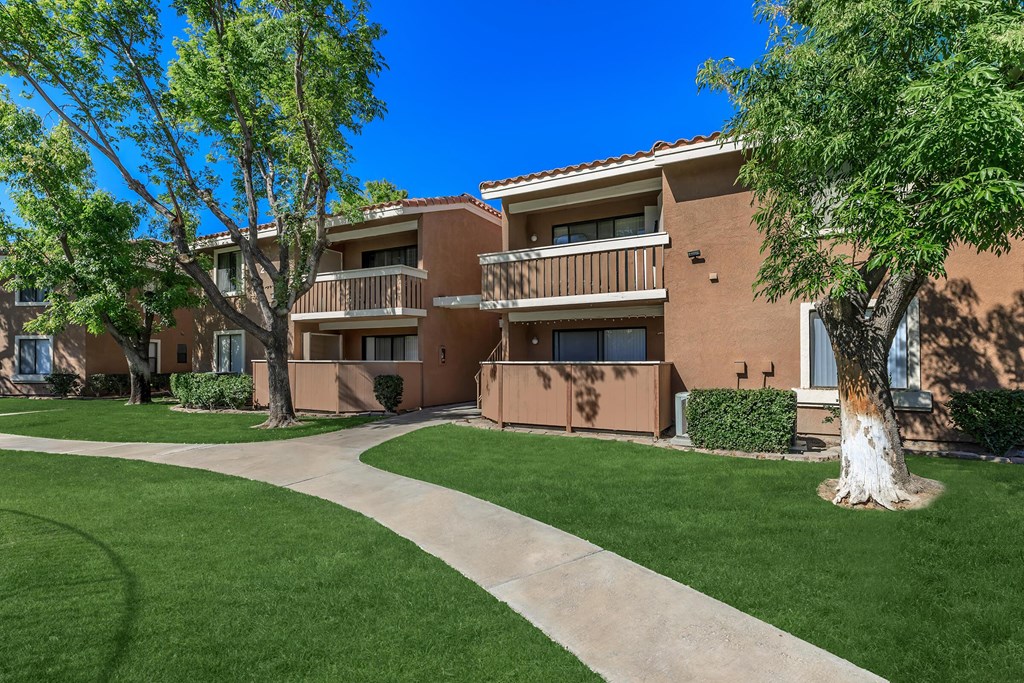 an apartment building with green grass and trees and a sidewalk