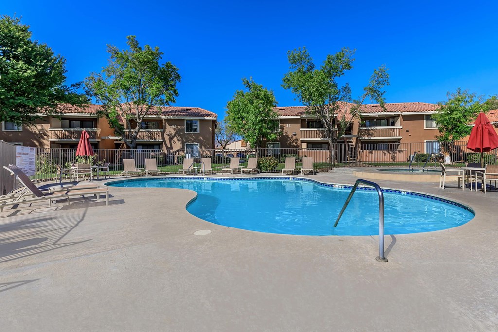 a swimming pool with chairs and umbrellas in front of apartment buildings