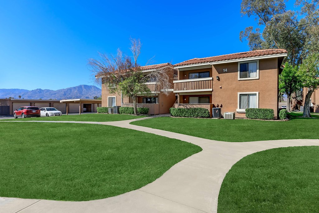 a sidewalk in front of an apartment building with green grass