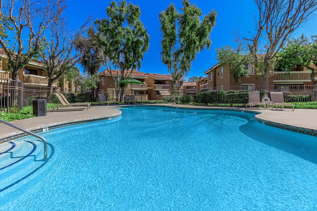 a large swimming pool with trees and apartments in the background