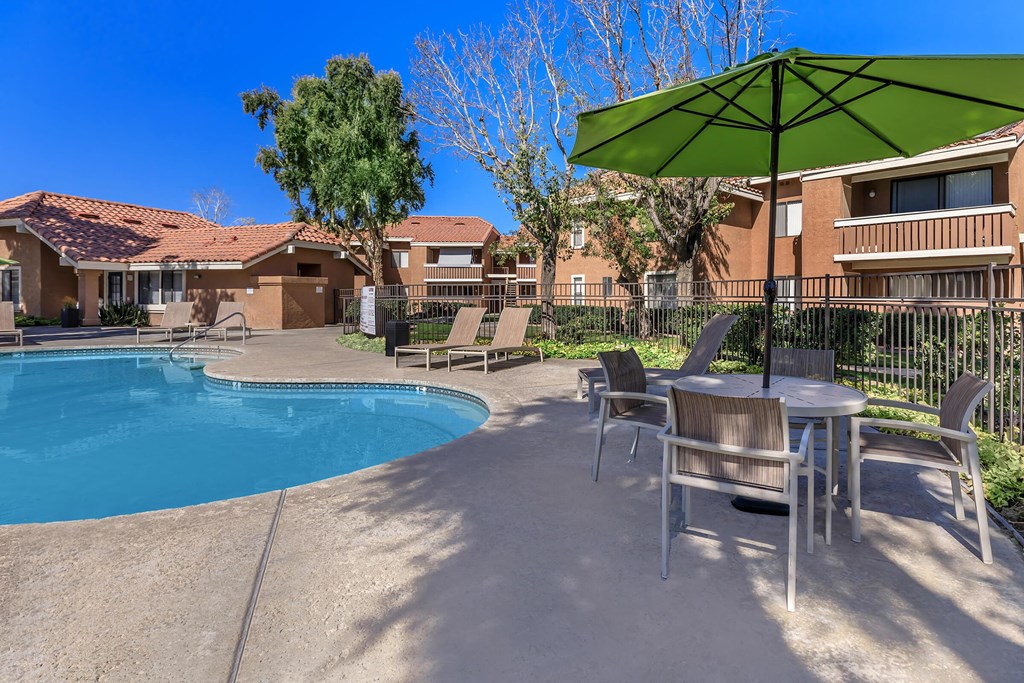 our apartments have a swimming pool and a patio with chairs and an umbrella