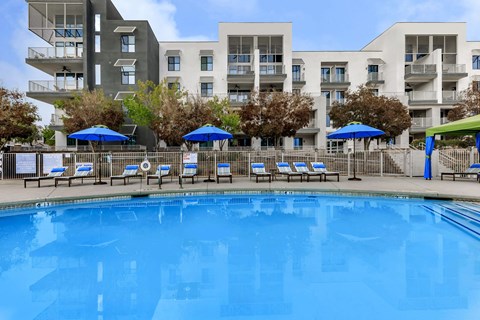 a large pool with chairs and umbrellas in front of an apartment building