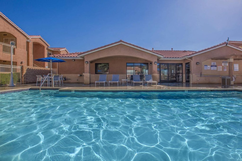 A swimming pool in front of a building with a blue umbrella.