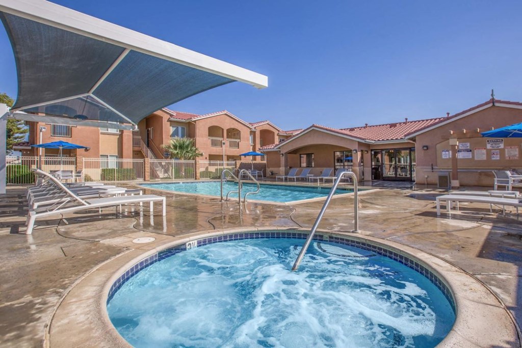 A hot tub sits in the middle of a pool surrounded by chairs and a building in the background.