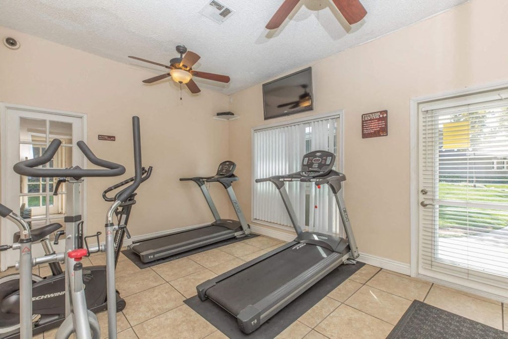 the gym has plenty of exercise equipment and a ceiling fan