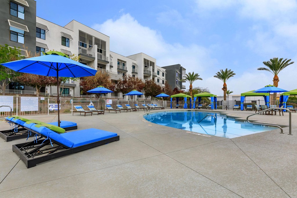 a swimming pool with lounge chairs and umbrellas in front of an apartment building