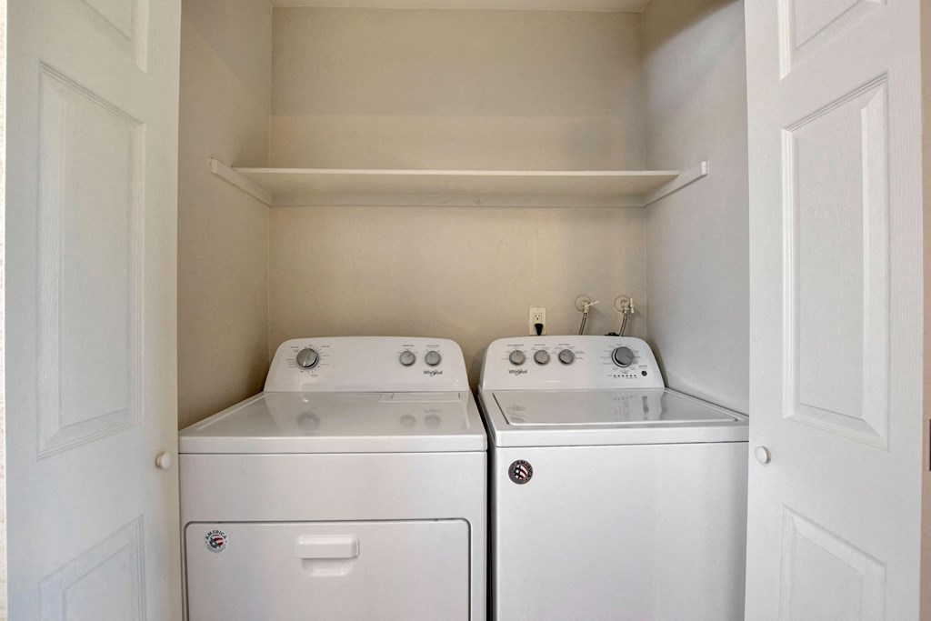 a washer and dryer in an empty laundry room with a shelf above it