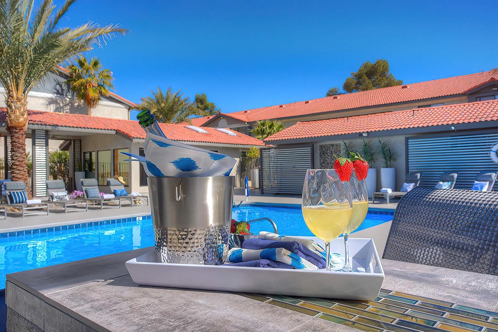 a poolside table with two glasses of wine and a cocktail