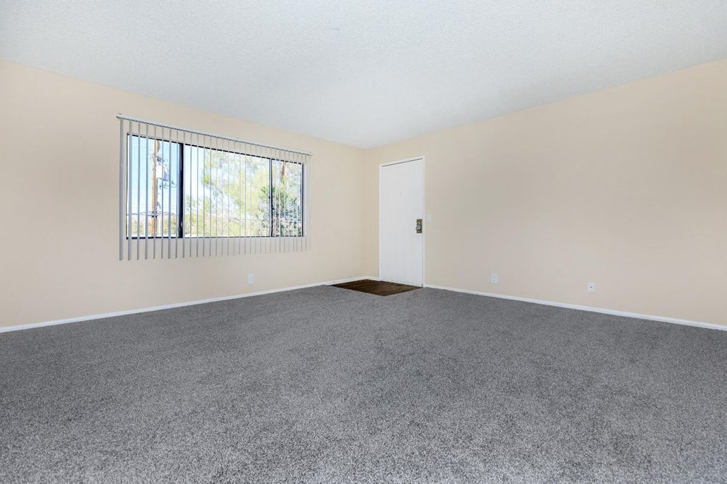 A room with a grey carpet and a window with bars.