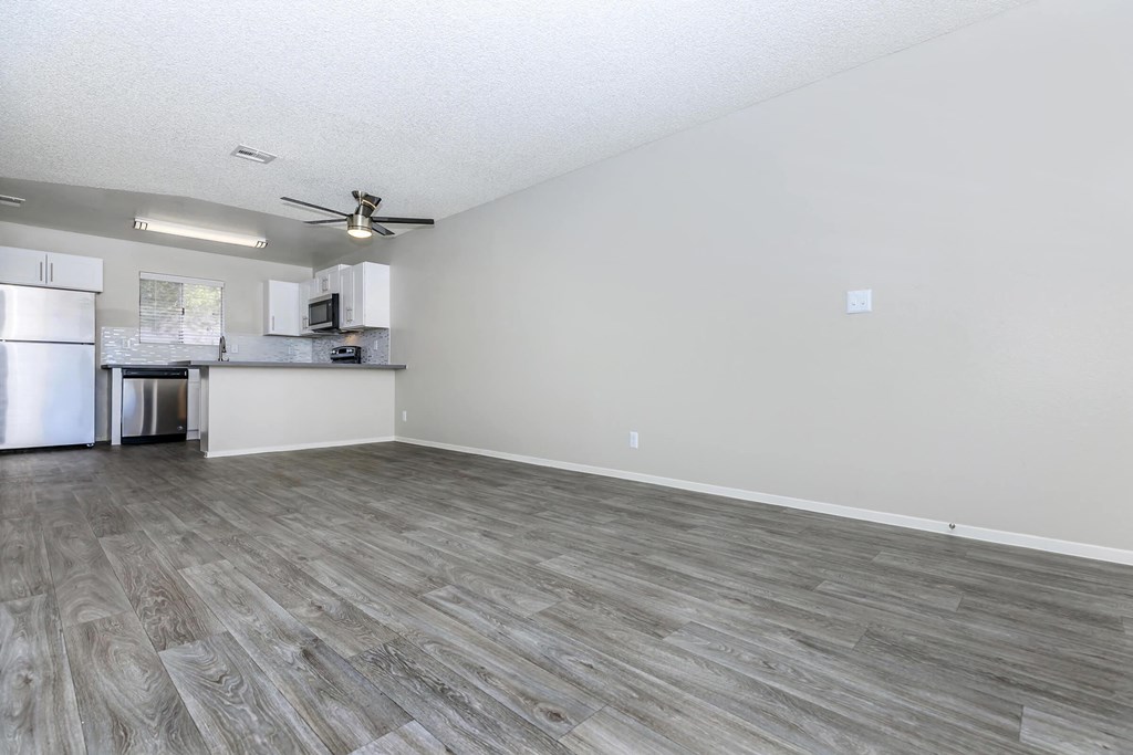 an empty living room with a kitchen and a ceiling fan