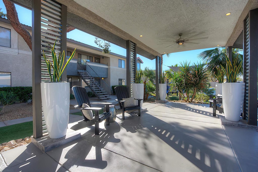 a covered patio with chairs and potted plants