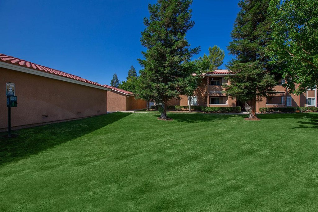 a yard with green grass and trees in front of a building