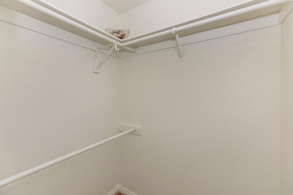 a walk in closet with white walls and a white rail on the ceiling