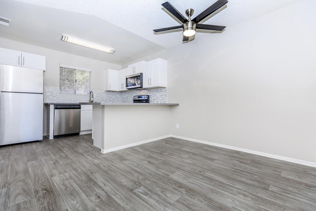 an empty living room with a kitchen and a ceiling fan