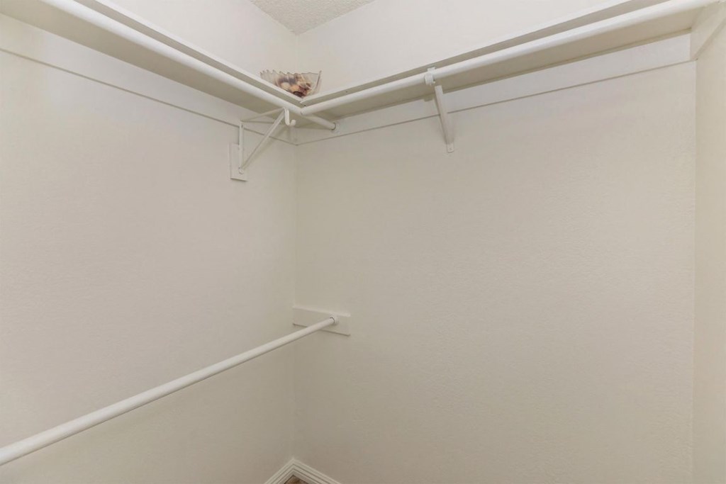 a white walk in closet with white walls and a white rail in the corner