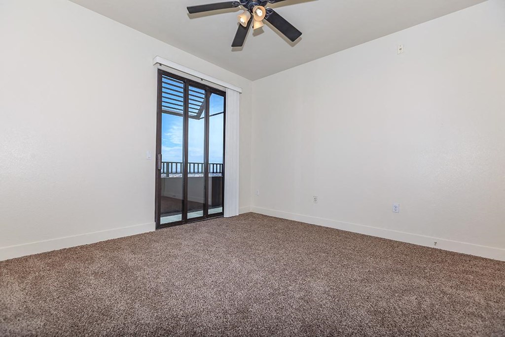 an empty living room with a ceiling fan and a balcony