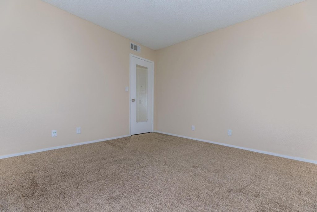 an empty living room with beige carpet and a white door