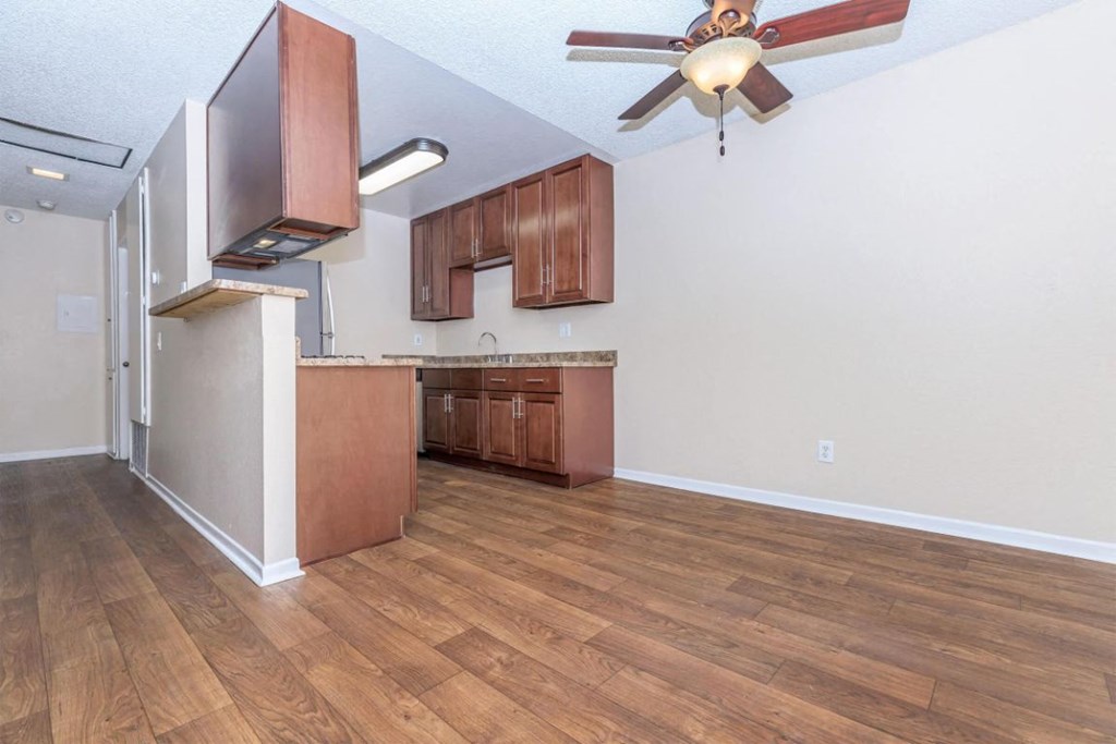 an empty living room with a kitchen and a ceiling fan