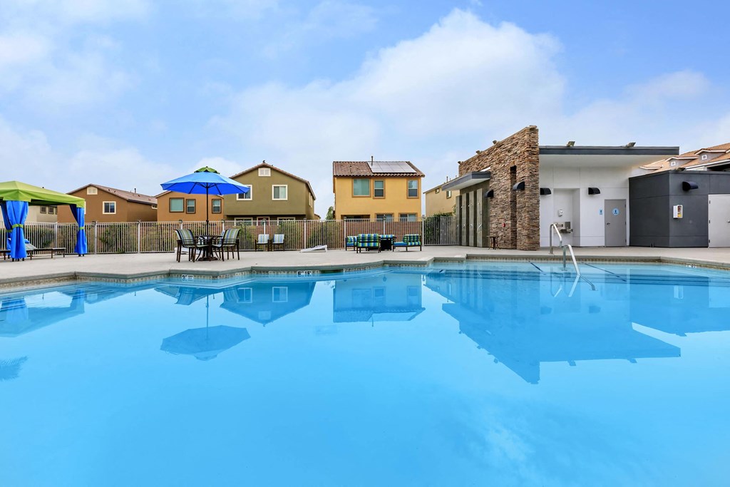 a swimming pool with tables and umbrellas in front of a house