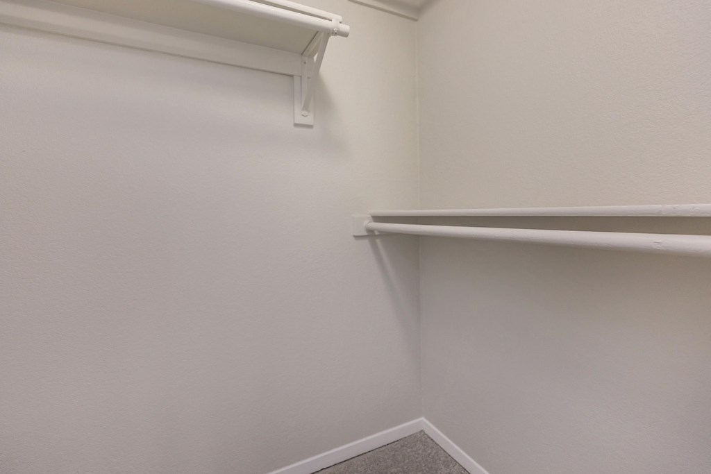 a walk in closet with a white wall and a hanging rack on the wall