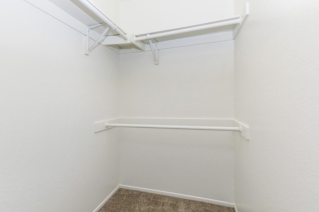 a walk in closet with white walls and a white shelf