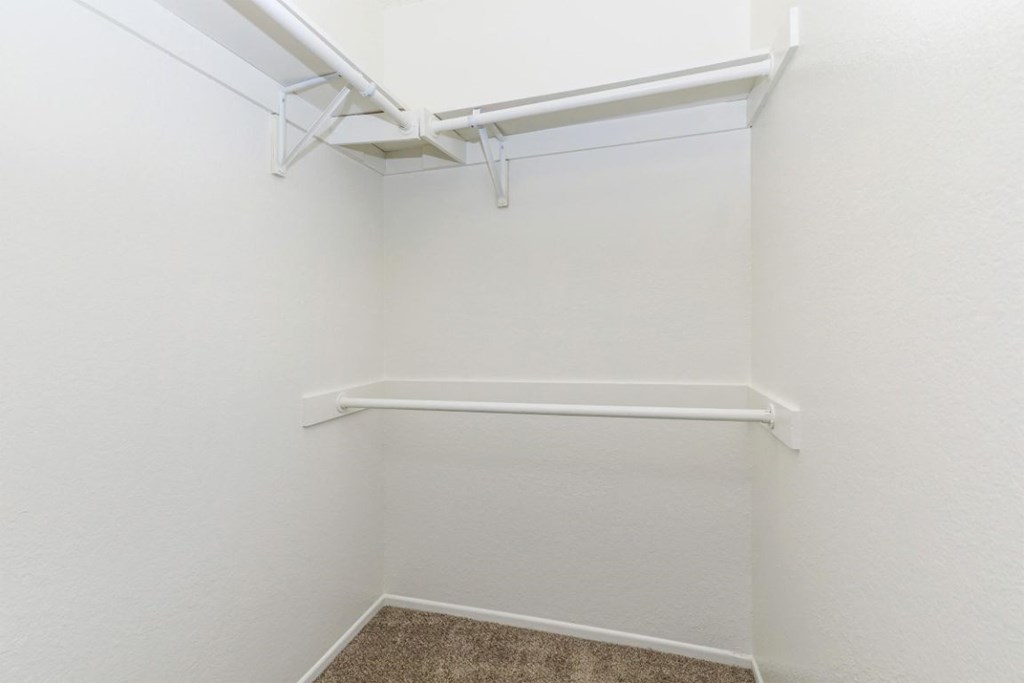 a walk in closet with a white wall and a shelf