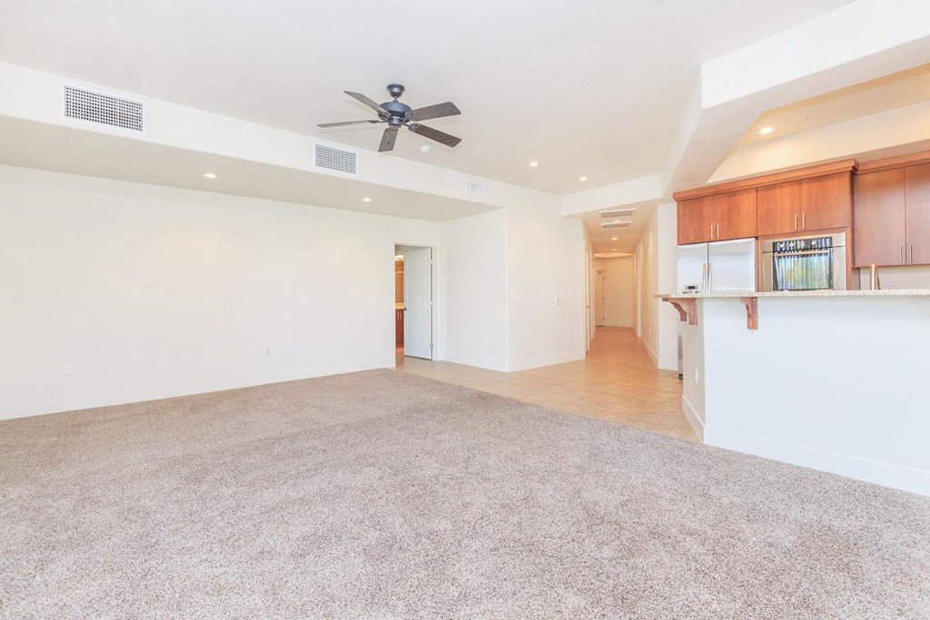 an empty living room with a ceiling fan and a kitchen
