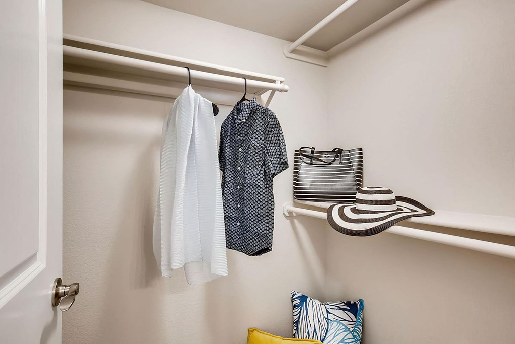 a walk in closet with clothes and a hat on a rack