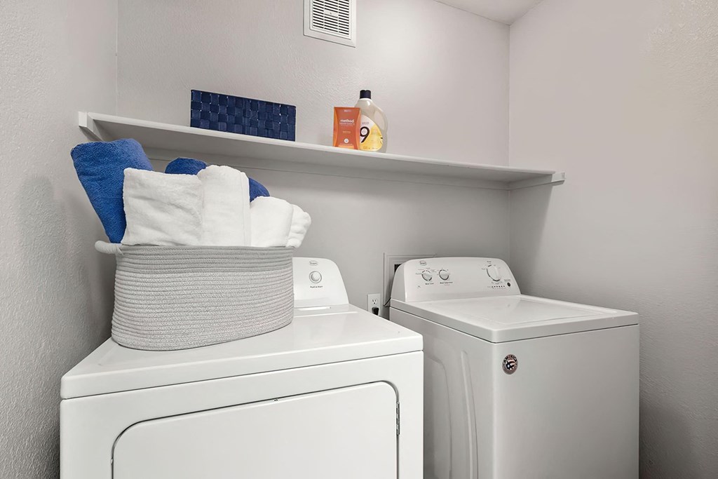 a white washer and dryer in a white room with a shelf on top